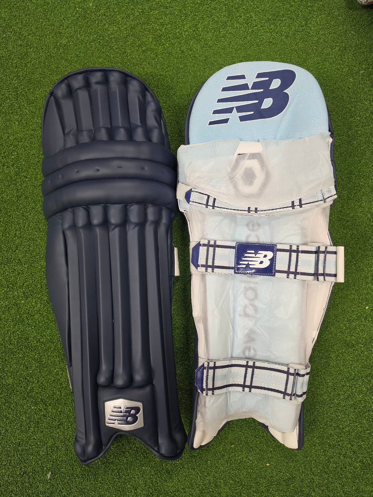 New Balance TC 8i cricket batting pad shown next to a matching navy blue protective pad cover clad on green turf.