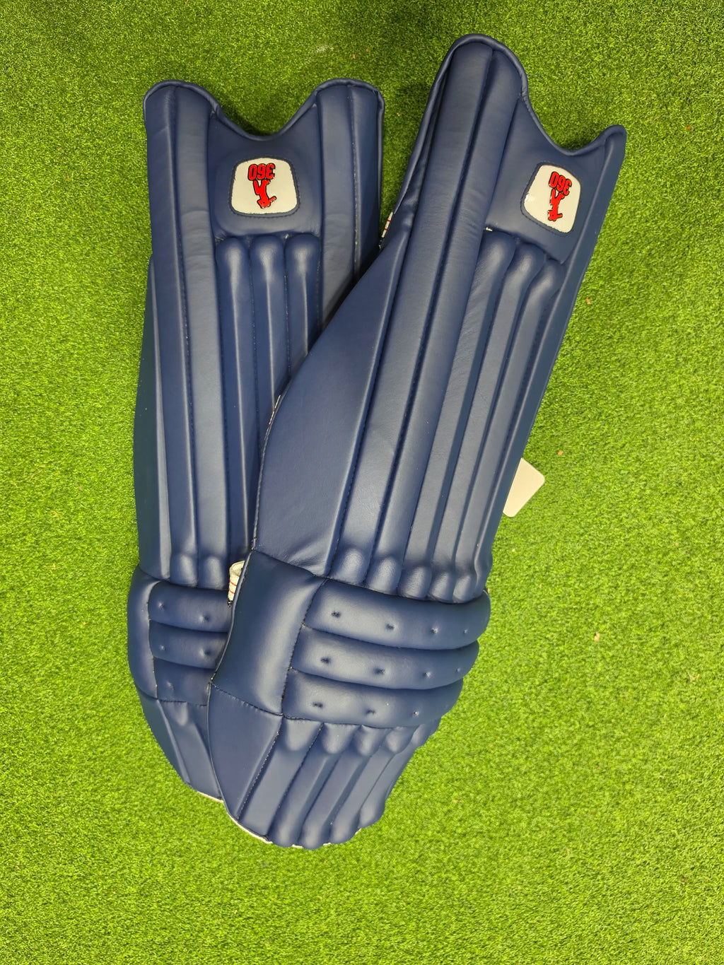 Top face view of EM 360 Bold adult navy blue cricket batting pads on artificial grass on Alberta.