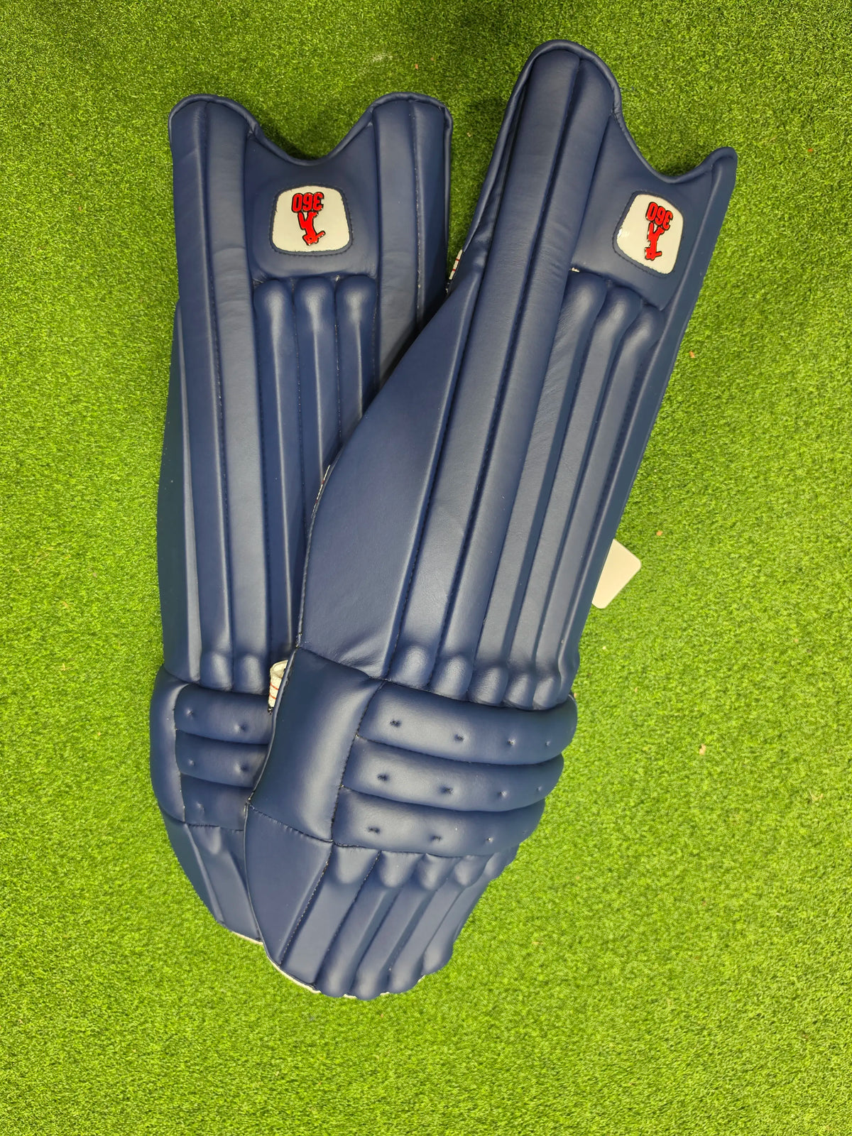 Top face view of EM 360 Bold adult navy blue cricket batting pads on artificial grass on Alberta.