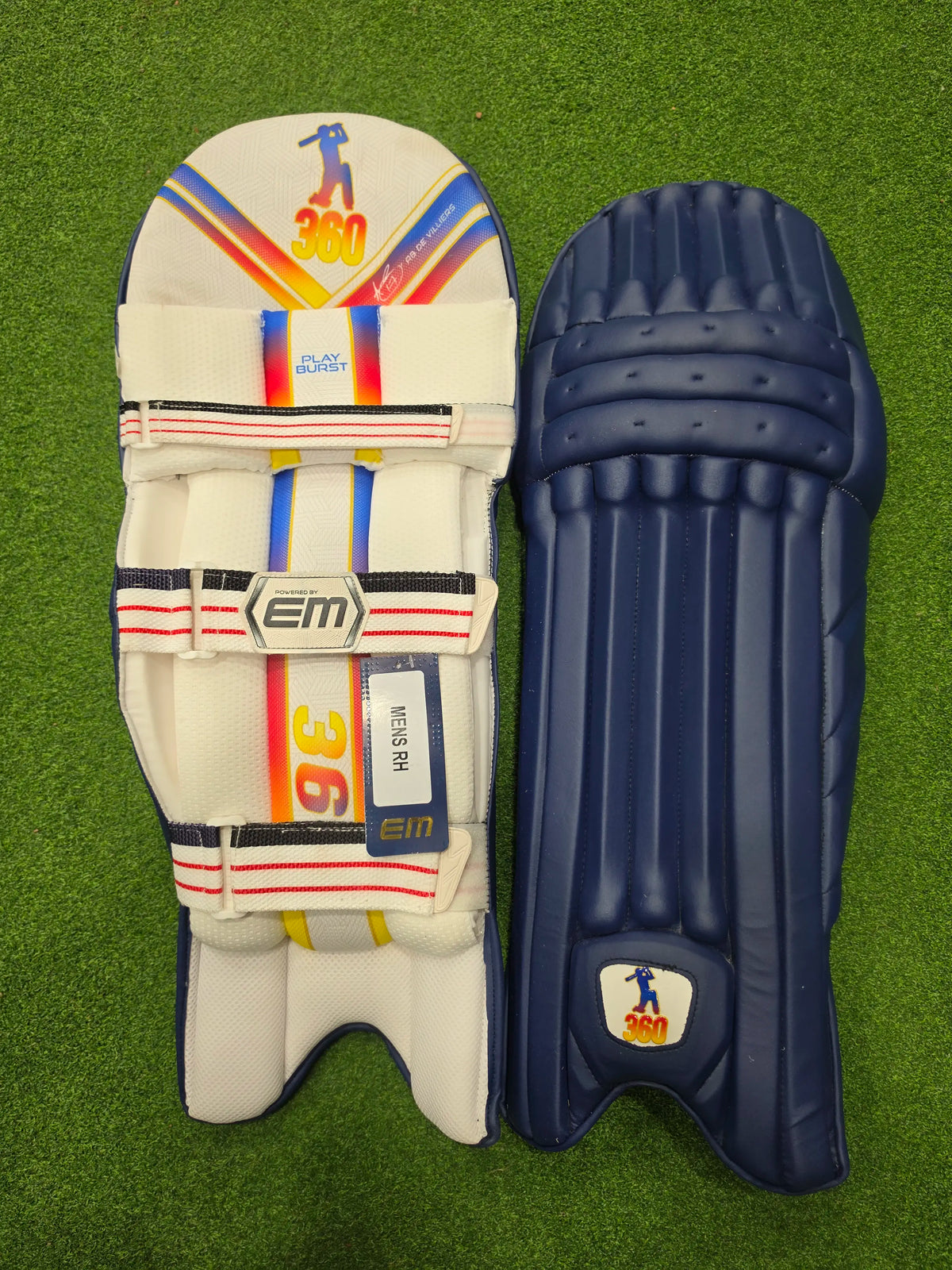 Front face and inner padded back view of EM 360 PLAY BURST adult navy blue cricket batting pads on artificial grass on Alberta.
