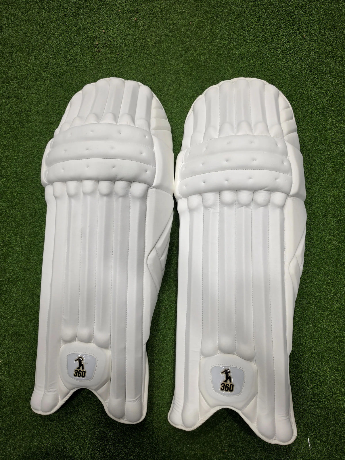Top view of EM 360 No 17 adult white cricket batting pads on green artificial grass on Alberta.