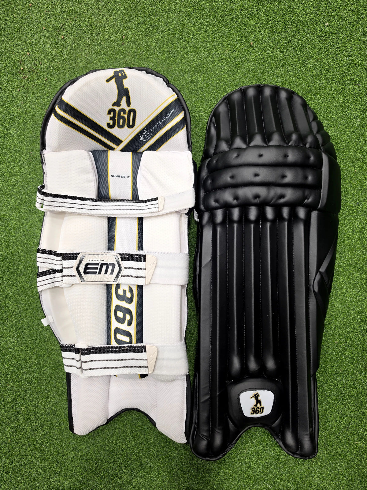 Front and back view of EM 360 No 17 black adult cricket batting pads placed on artificial grass on Alberta.