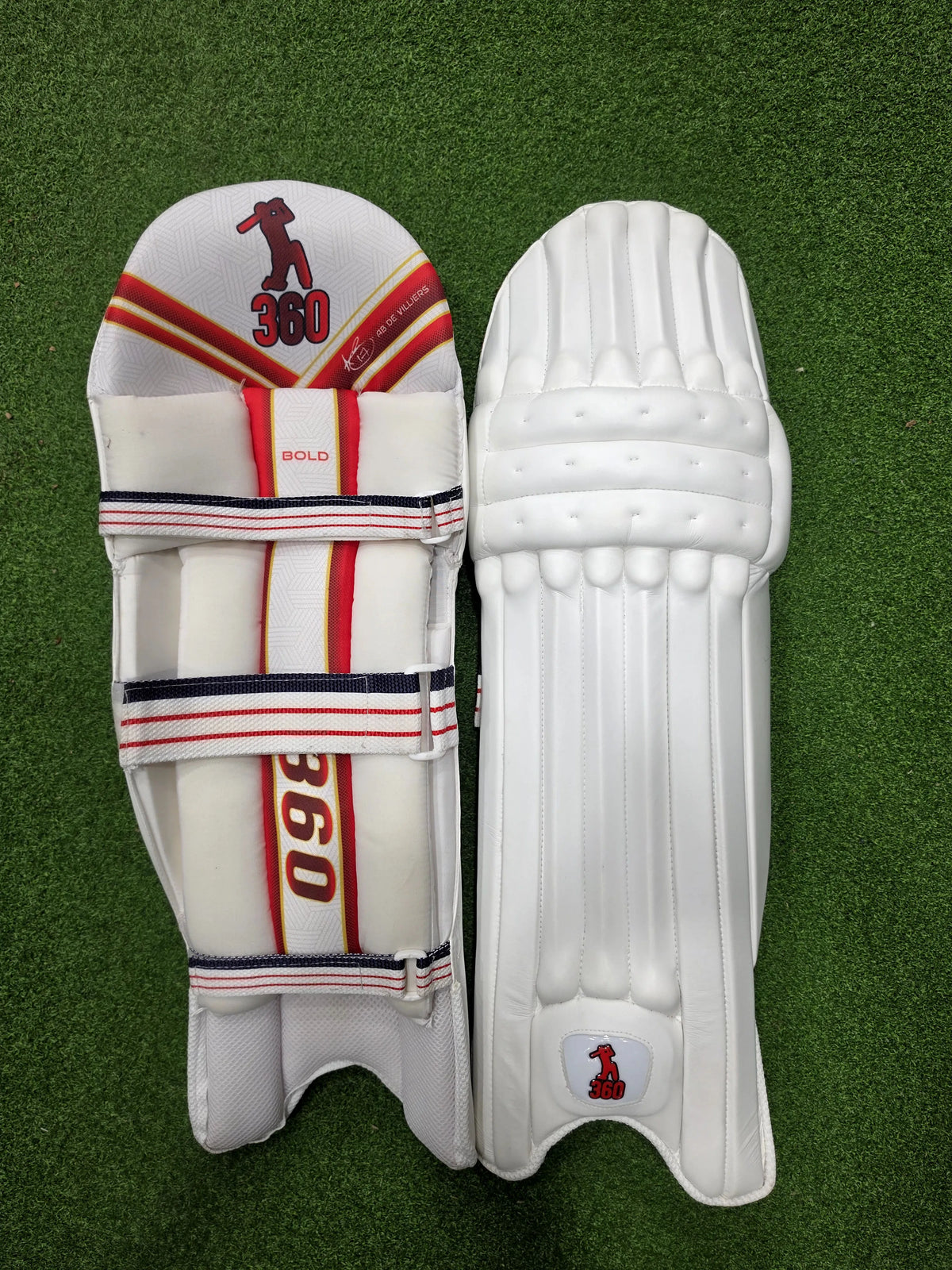 Top face view of EM 360 Bull Ring adult navy blue cricket batting pads on artificial grass on Alberta.