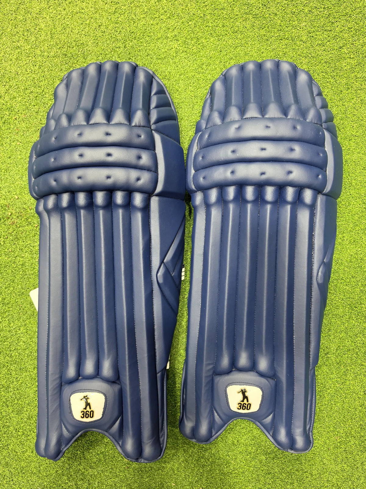 Top view of EM 360 No 17 adult navy blue cricket batting pads on artificial grass on Alberta.