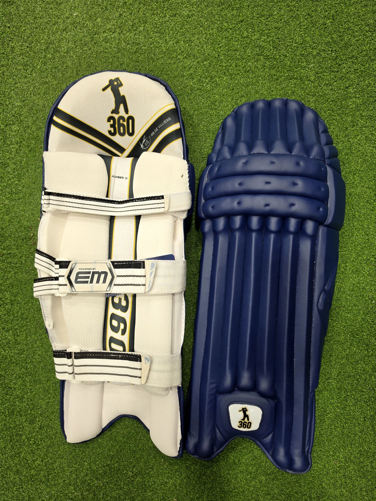 Front and back view of EM 360 No 17 navy blue adult cricket batting pads placed on artificial grass on Alberta.